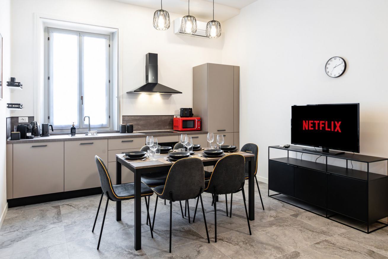 A modern kitchen with a dining area, a TV, and a clock on the wall.