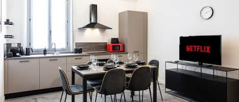 A modern kitchen with a dining area, a TV, and a clock on the wall.