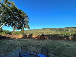 Ein Garten mit einer Holzterrasse, zwei Metallstühlen und einem großen Baum.