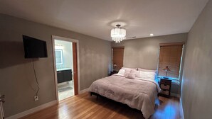 Ein Schlafzimmer mit einem Bett, einer Kristalllüster, einem Fernseher und einem Fenster mit Jalousien.