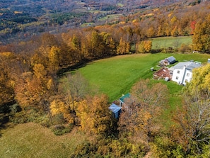 Eine Luftaufnahme eines ländlichen Anwesens mit einem großen grünen Feld, einem weißen Gebäude mit einem grünen Dach und umliegenden Bäumen im Herbstlaub.