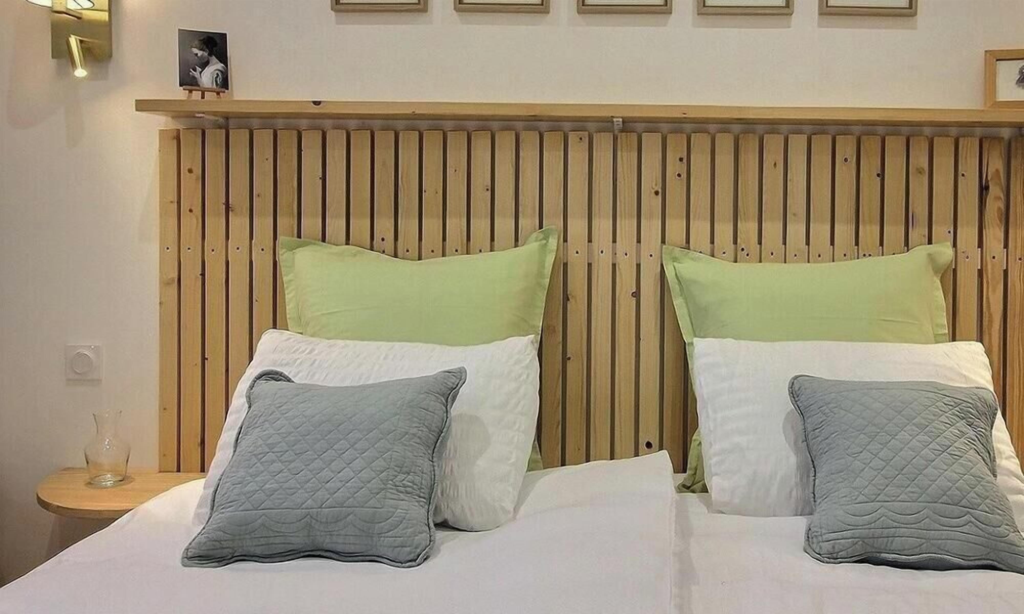 Una cama con cabecera de madera, dos almohadas verdes y dos almohadas grises.