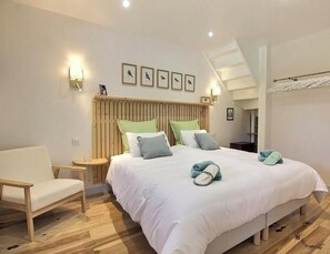 Ein Schlafzimmer mit Bett, einem Sessel, einem Nachttisch, einer Wandlampe und einer Treppe.