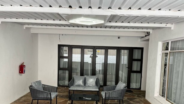 A covered patio with stone flooring, a sofa, two chairs, and a fire extinguisher. - Room-makays Guests House Kimberley (Kimberley)