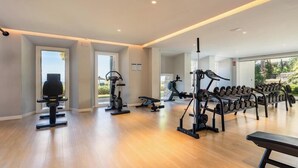 Ein geräumiger Fitnessraum mit Trainingsgeräten, großen Fenstern und Holzboden.