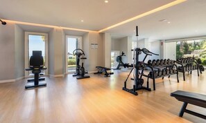Ein geräumiger Fitnessraum mit Trainingsgeräten, großen Fenstern und Holzboden.