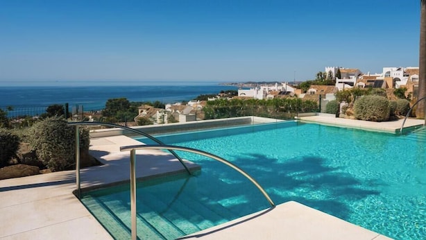 Ein Schwimmbecken mit klarem, blauem Wasser, umgeben von einer gefliesten Terrasse und einem Metallgeländer.