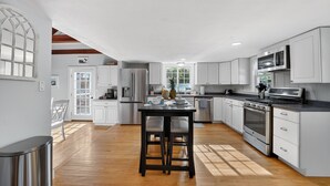 Una cocina moderna con armarios blancos, una isla central, electrodomésticos de acero inoxidable y suelo de madera.