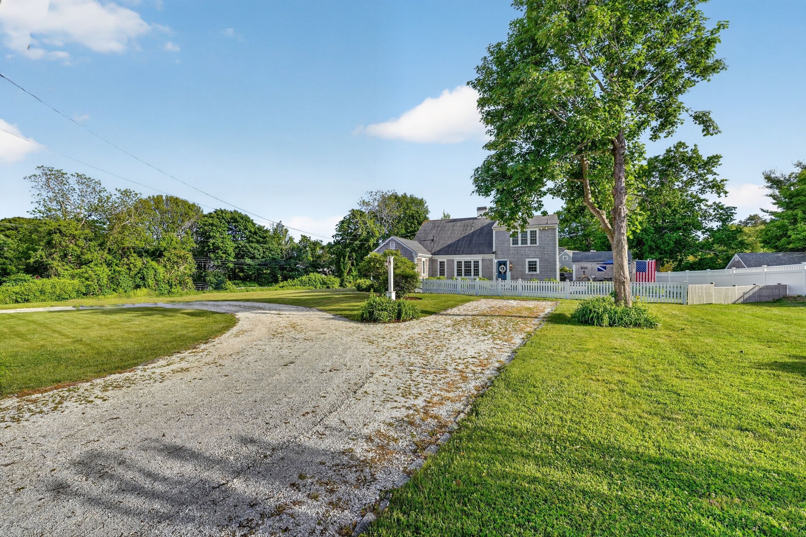 A residential property with a gravel driveway, a lawn, and a large house with a porch.