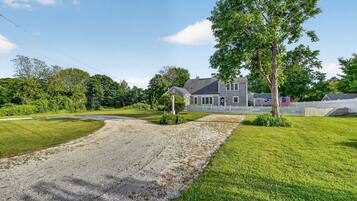 A residential property with a gravel driveway, a lawn, and a large house with a porch.