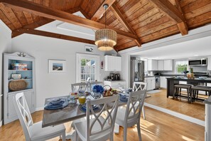 A spacious kitchen with wooden beams, white cabinets, and a dining area with a table set for four. - East Dennis Gem! Walk to Beach! Sleeps 10! (Dennis)