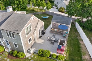 A two-story house with a deck, outdoor seating, and a flag. - East Dennis Gem! Walk to Beach! Sleeps 10! (Dennis)