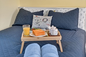 A bed with a quilted blue bedspread, a tray with breakfast including toast, fruit, and a glass of orange juice, and a pillow with nautical designs. - East Dennis Gem! Walk to Beach! Sleeps 10! (Dennis)