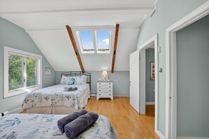 A bedroom with two beds, a skylight, a bedside table with a lamp, and a window with blinds. - East Dennis Gem! Walk to Beach! Sleeps 10! (Dennis)