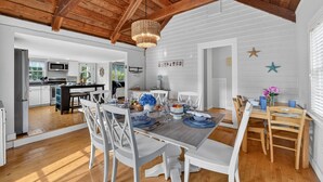 Comedor con una mesa de madera dispuesta para seis personas, sillas blancas y una lámpara de araña.