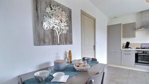 A dining area with a table set for two, a decorative tree artwork on the wall, and a modern kitchen in the background. - A good mood - PLEUBIAN (PLEUBIAN)