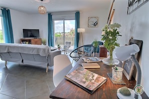 Ein Wohnzimmer mit einer Couch, einem Esstisch mit einer Zeitschrift, einer Pflanze und einem Föhn.
