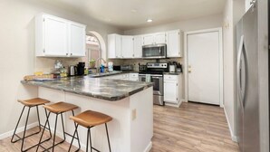 Una cocina con armarios blancos, encimera de granito, refrigerador de acero inoxidable y horno empotrado.