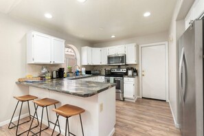 A kitchen with white cabinets, a granite countertop, a stainless steel refrigerator, and a built-in oven. - Pool Home Near Cardinals | Great for Families (Peoria)