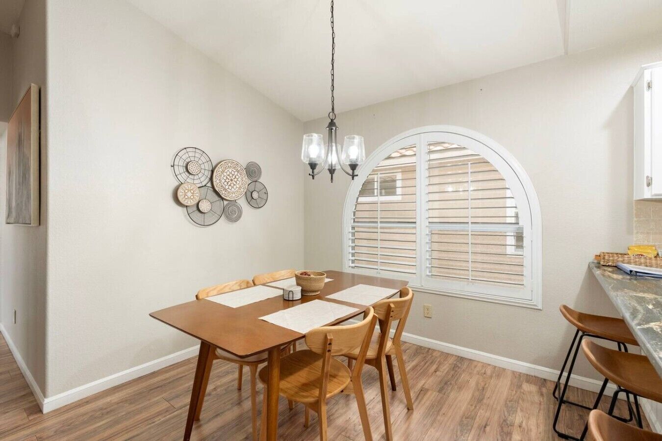 A dining area with a wooden table, chairs, a chandelier, and a window with blinds.
