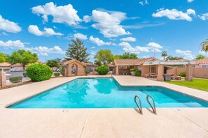 A rectangular swimming pool with two ladders, surrounded by a patio area with outdoor furniture, under a clear blue sky. - Pool Home Near Cardinals | Great for Families (Peoria)