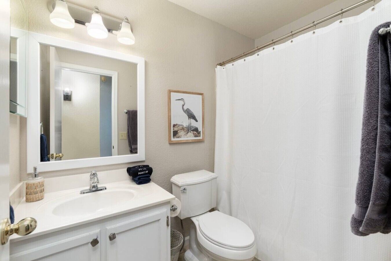 A bathroom with a white sink, mirror, toilet, and shower curtain.
