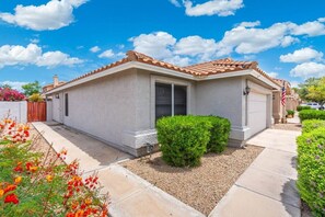 A single-story house with a tiled roof, a front door, and a small front yard with a bush and flowers. - Pool Home Near Cardinals | Great for Families (Peoria)