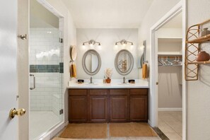 A bathroom with a glass shower enclosure, a double vanity with two mirrors, and a wall-mounted light fixture. - Pool Home Near Cardinals | Great for Families (Peoria)