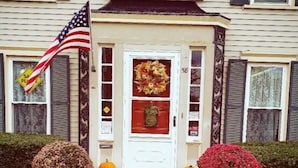 A building with a sign reading 'YWCA' above the entrance, a white door with a wreath, two potted plants on either side, and an American flag to the left.