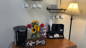 A coffee station with a sign, mugs on hooks, a lamp, and a date display.