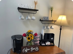 A coffee station with a sign, mugs on hooks, a lamp, and a date display.