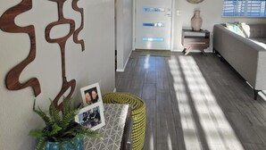 Ein modernes Wohnzimmer mit einem grauen Sofa, Wanddeko aus Holz, einer Topfpflanze und einem kleinen Tisch mit Bilderrahmen.