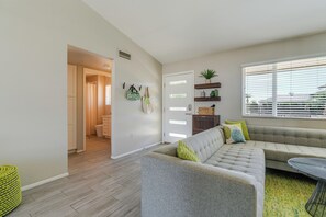 A modern living room with a grey sectional sofa, a small table, and a window with blinds. - Beautiful Mid Century Modern 2/2 with resort style backyard in Sun City West (Sun City West)