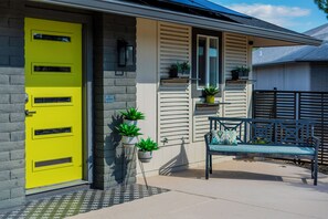 A house with a bright yellow door, a bench with cushions, and potted plants on the porch. - Beautiful Mid Century Modern 2/2 with resort style backyard in Sun City West (Sun City West)