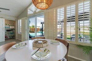 A dining area with a round table, chairs, and a view of a swimming pool through large windows. - Beautiful Mid Century Modern 2/2 with resort style backyard in Sun City West (Sun City West)