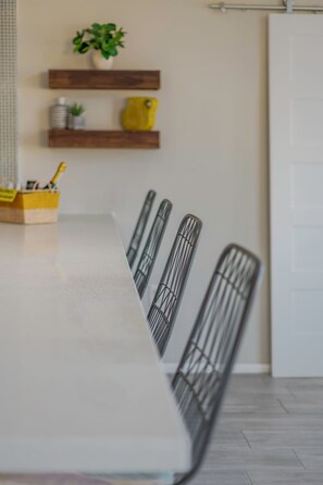 A dining area with a long table, chairs, and a plant on a shelf. - Beautiful Mid Century Modern 2/2 with resort style backyard in Sun City West (Sun City West)
