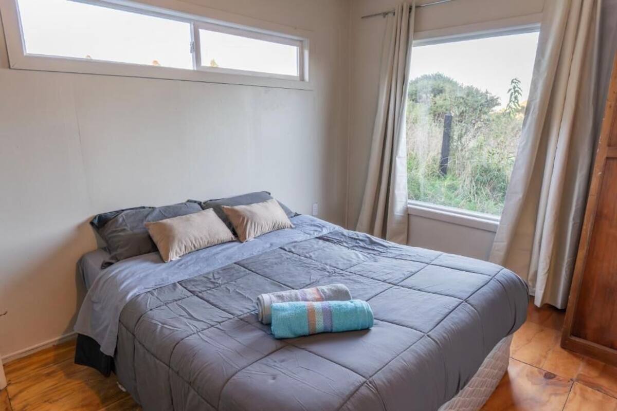 A bedroom with a bed, two windows, and a view of greenery.