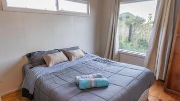 Une chambre à coucher avec un lit, deux fenêtres et une vue sur la verdure.