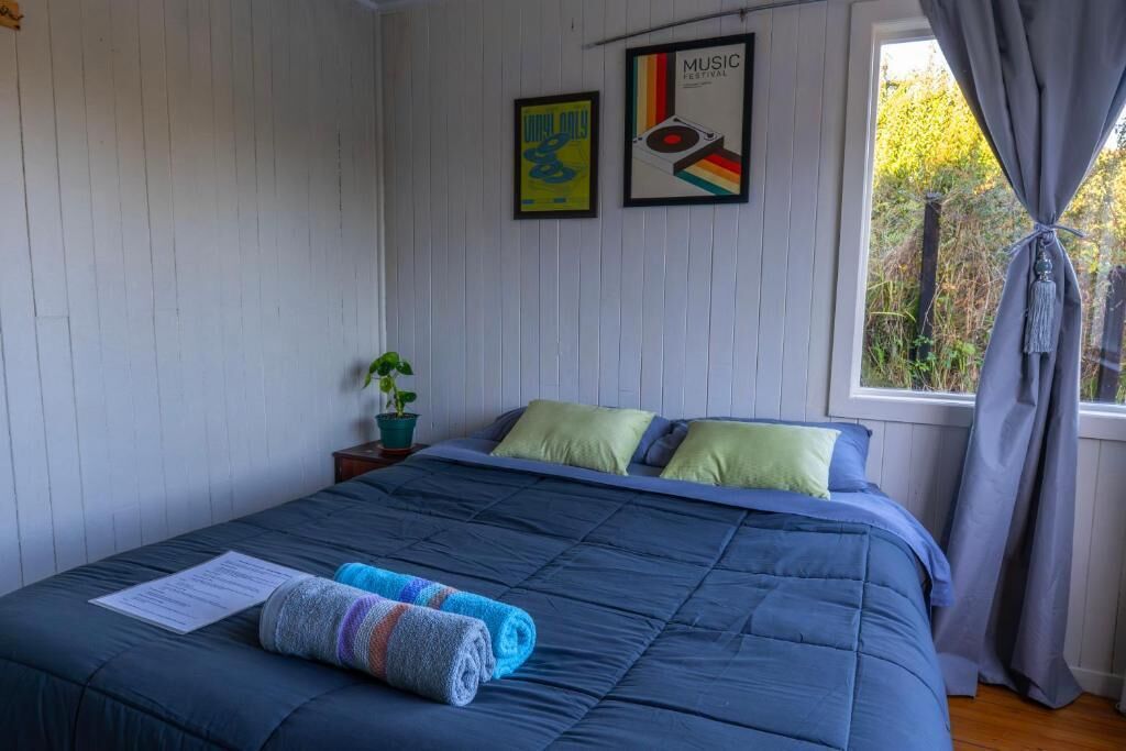 Ein Schlafzimmer mit Bett, einem Fenster mit Vorhängen, einer Blumentopfpflanze und zwei gerahmten Postern an der Wand.