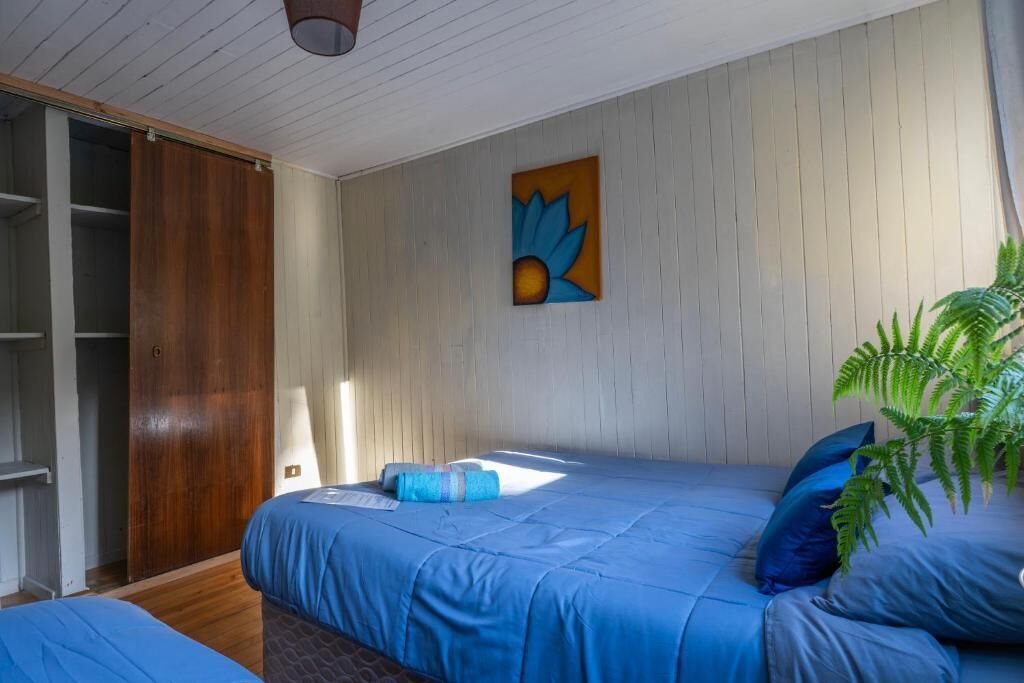 A bedroom with a bed, a wooden wardrobe, a painting, and a potted plant.