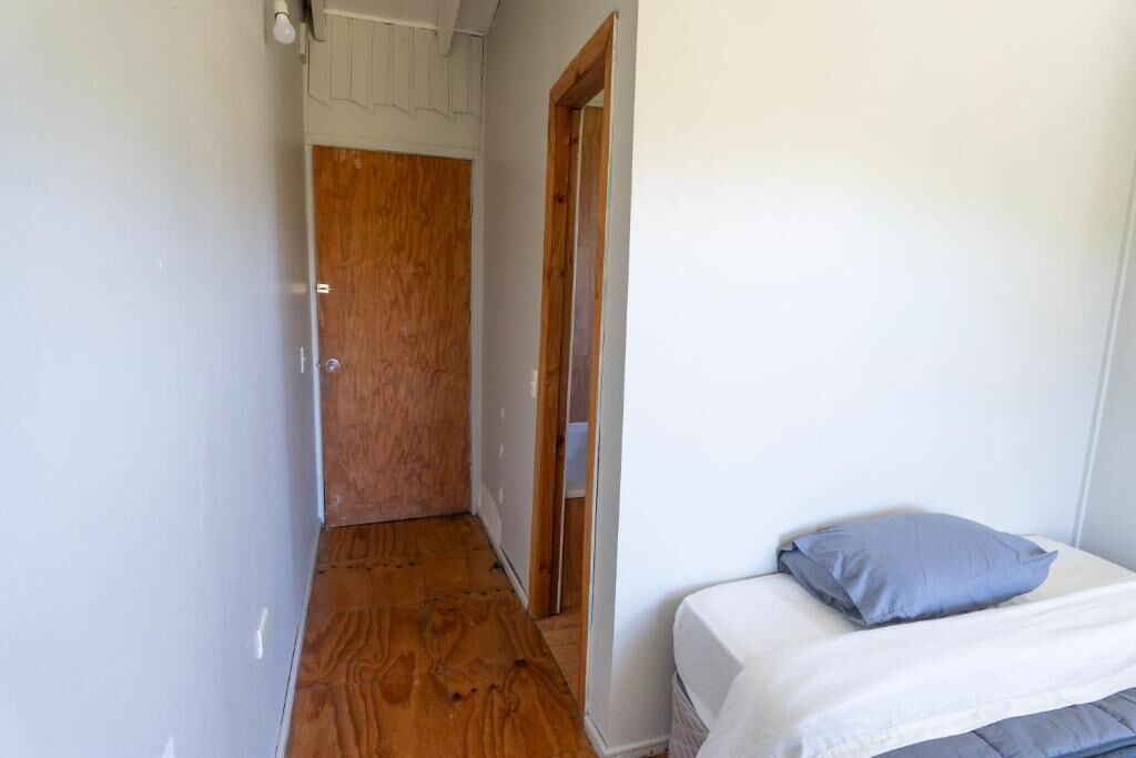 A narrow hallway with wooden flooring, a white door at the end, and a bed with a blue pillow.
