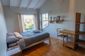 Makuuhuoneessa on sänky, puinen työpöytä, tuoli, ikkuna, jossa on verhot, ja hylly, jossa on kasveja.