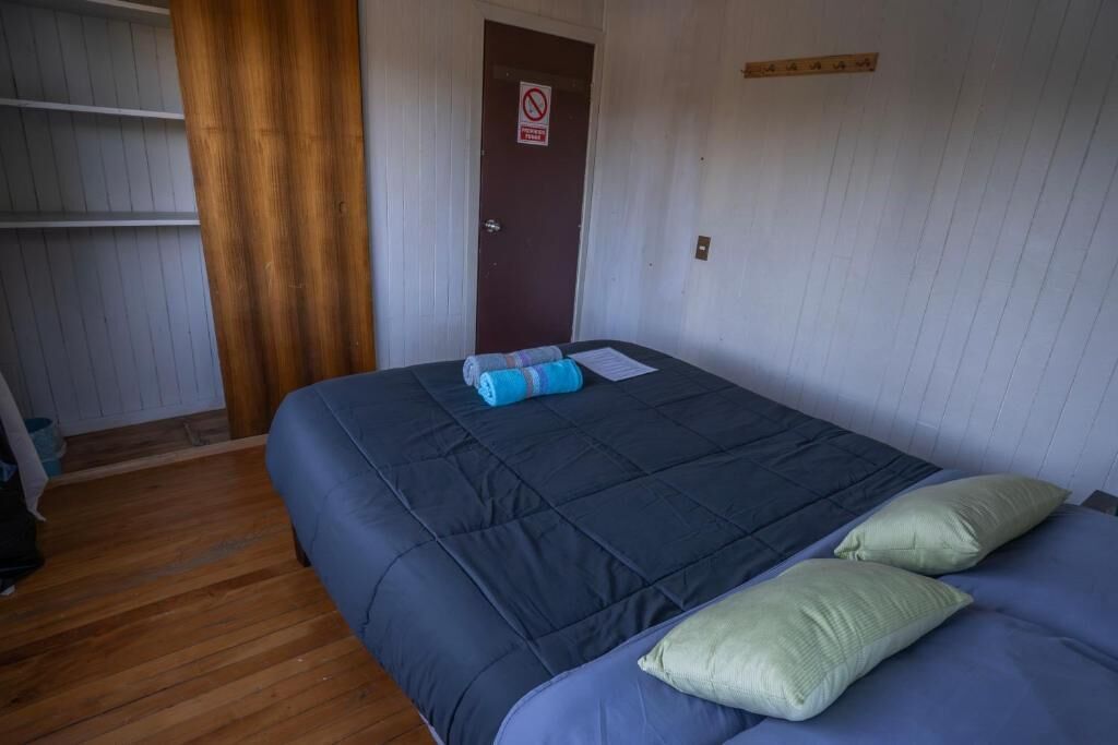 Una habitación con una cama, una puerta con el cartel de prohibido fumar y un suelo de madera.