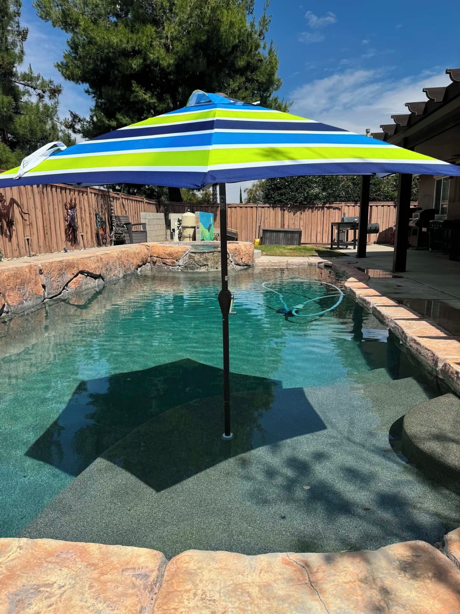 Una piscina amb una ombra d'estriades, un marc de pedra i una tanca de fusta al fons.