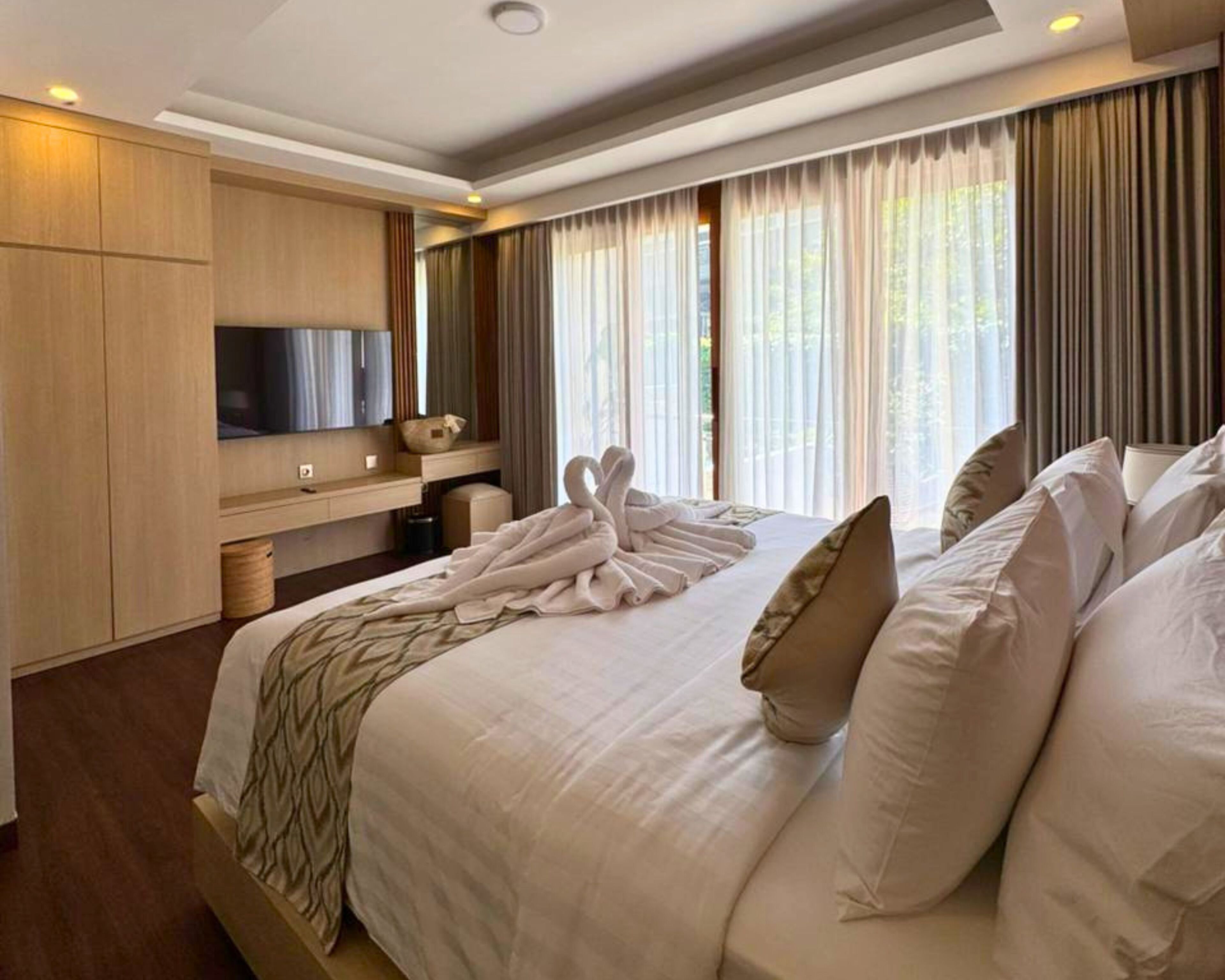 Ein Hotelzimmer mit einem großen Bett, einem Flachbildfernseher, einer Holzkommode und einem Fenster mit Vorhängen.