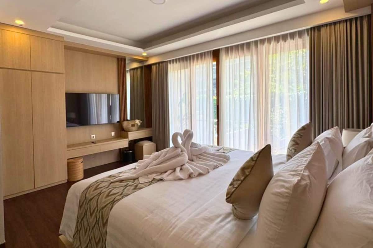 A hotel room with a large bed, a flat-screen TV, a wooden cabinet, and a window with curtains.