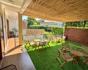 Eine Terrasse im Freien mit Kunstgrras, Korbmöbeln und einer Glasreling.
