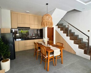 Eine moderne Küche mit Holzschränken, einem schwarzen Kühlschrank und einem Essbereich mit Tisch und Stühlen.