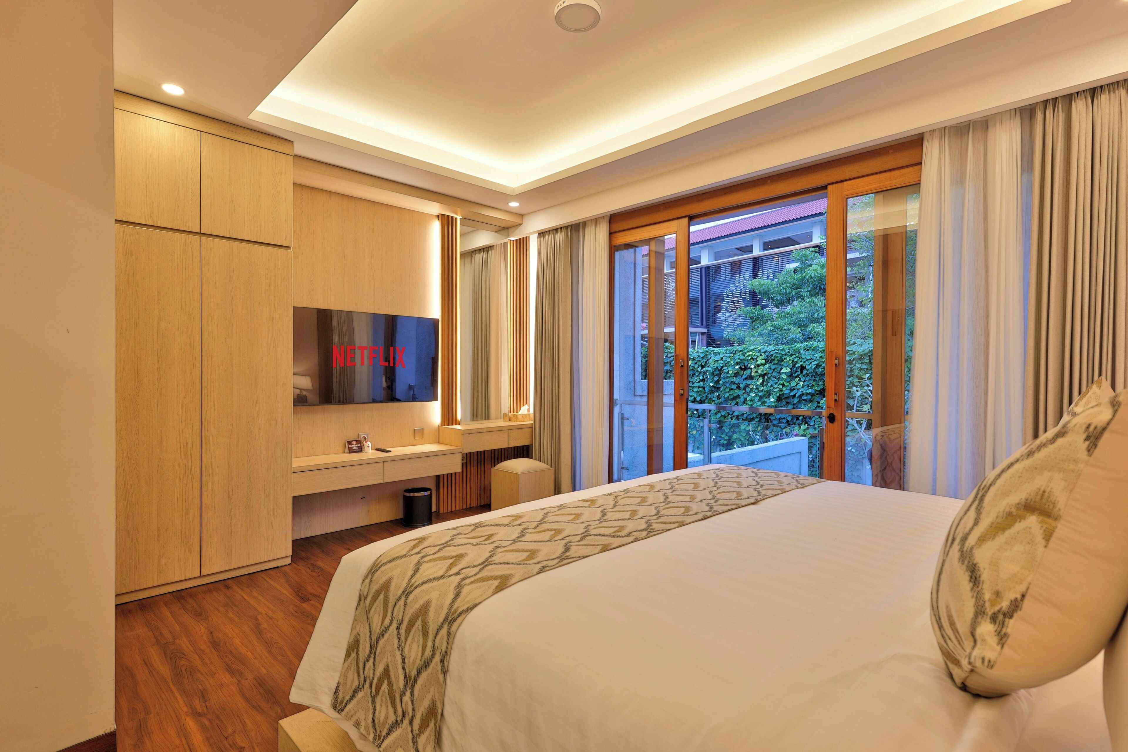 Habitación de hotel con cama, televisión, escritorio y balcón con vistas.