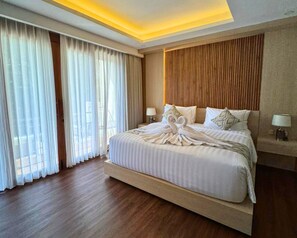 Ein Hotelzimmer mit einem großen Bett, Holzboden, einem Holzkopfende und Blick durch leichte Vorhänge.